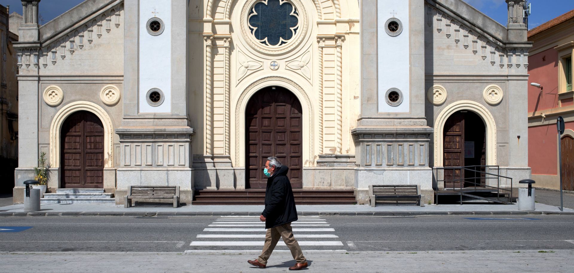 A man wearing a protective mask walks in the empty square in front of a cathedral in Locri, Italy, on April 7, 2020.