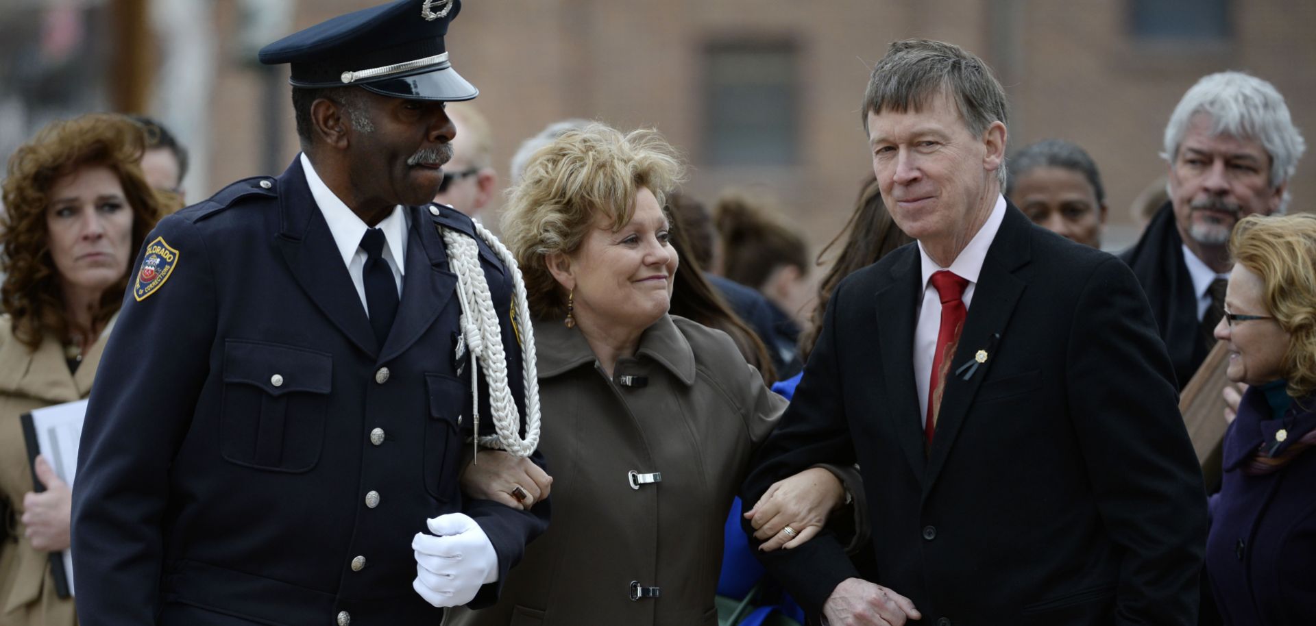 Lisa Clements (C), wife of fallen Department of Correction executive director, Tom Clements, cracks a half-smile as Colorado Department of Corrections Honor Guard member Harry Campbell (L) and Colorado Gov. John Hickenlooper escort her away from a memorial event in Canon City, Colorado, on March 15, 2014.