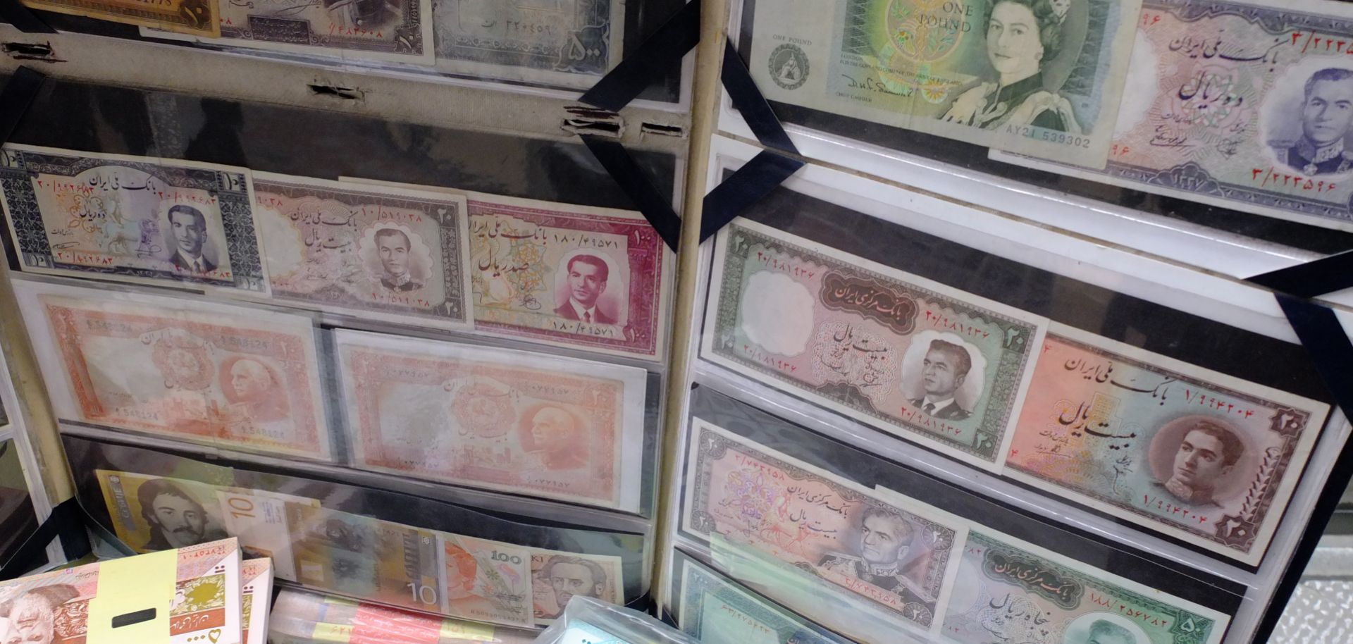 A brand new one Pound Sterling banknote issued bythe Bank of England with image of the Queen printed on it is displayed as collector's items on a sidewalk briefcase next to and old ten Rials bill issued by Bank Melli of Iran with the Shah's image for sale on May 3, 2013 in Tehran, Iran.