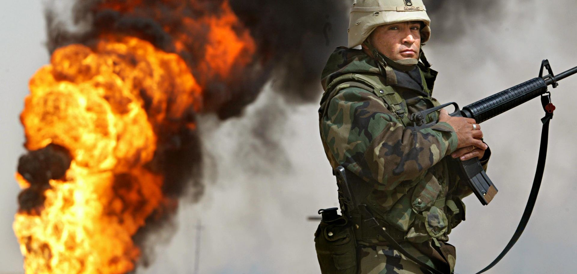 U.S. Army Staff Sgt. Robert Dominguez stands guard next to a burning oil well in the oil fields of Rumaila, Iraq, on March 27, 2003.