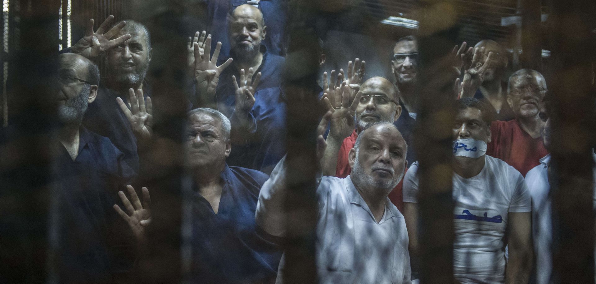 Egyptian Muslim Brotherhood senior members, including Khairat al-Shater (top left), gesture from the defendants' cage at the Egyptian Police Academy on the outskirts of Cairo on June 2, 2015. 