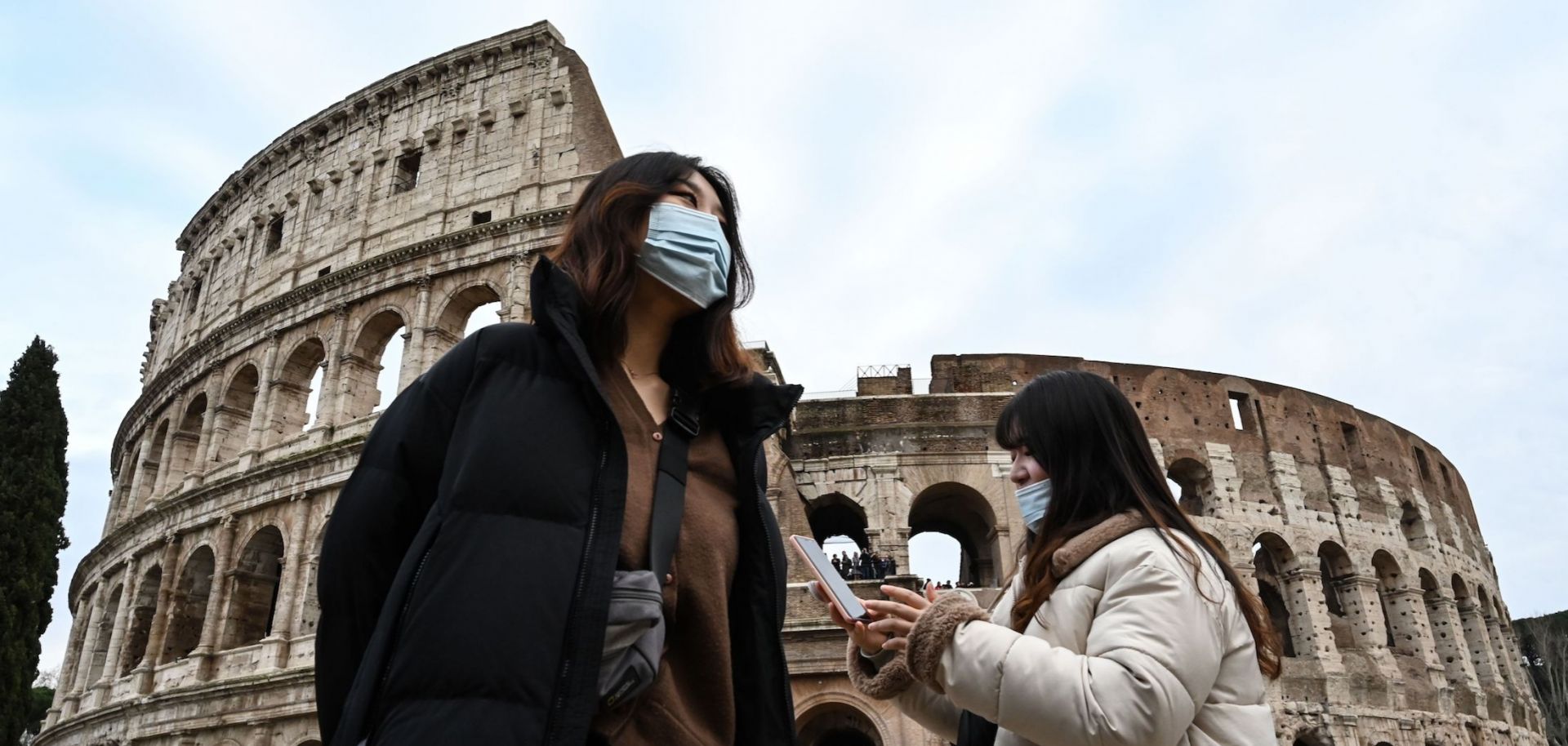 Two women wearing blue, protective respiratory masks take a tour outside the Colosseum in Rome, Italy, on Jan. 31, 2020, after two cases of the new coronavirus were confirmed in the city.