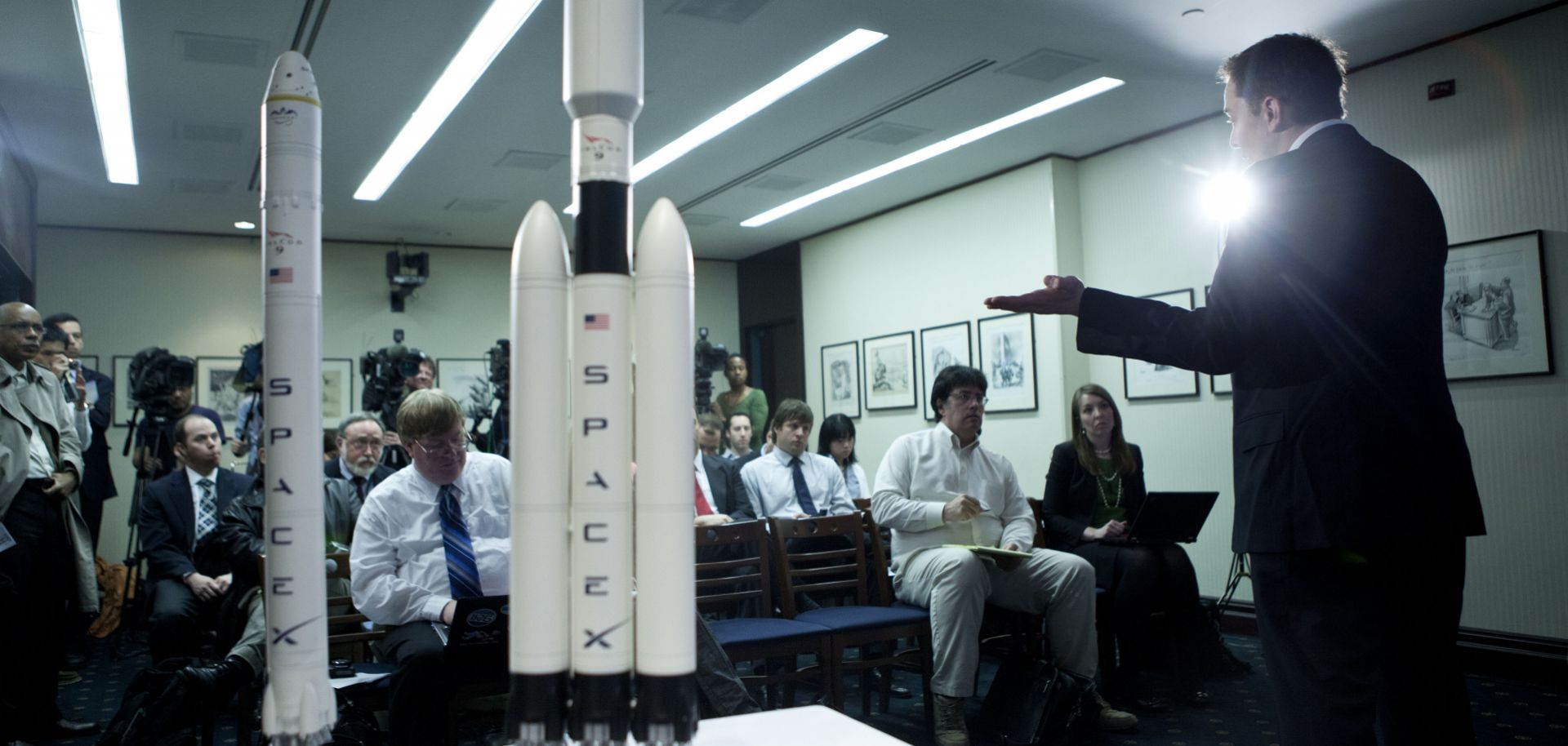 SpaceX CEO Elon Musk delivers a presentation while standing beside scale models of the rockets his company produces.