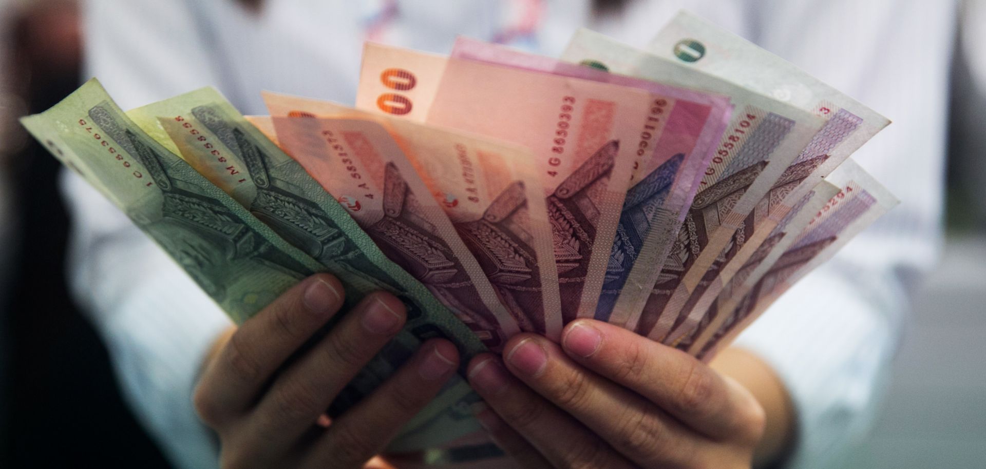 A bank teller counts Thai bhat before handing it to a customer in Bangkok.