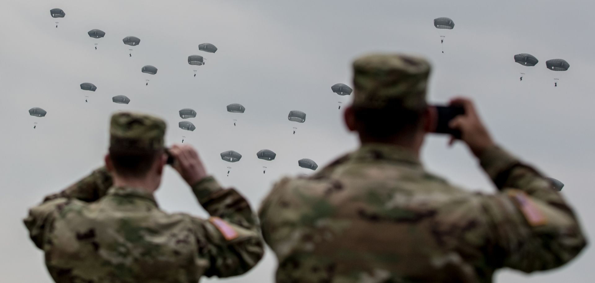 U.S. soldiers watch paratroopers from the U.S. Army 173rd Airborne Brigade, the UK's 16 Air Assault Brigade and Italian Folgore Airborne Brigade as they parachute to the ground during a training jump as part of the Saber Junction 16 military exercises near the Hohenfels Training Area. April 2016, near Grafenwoehr, Germany.