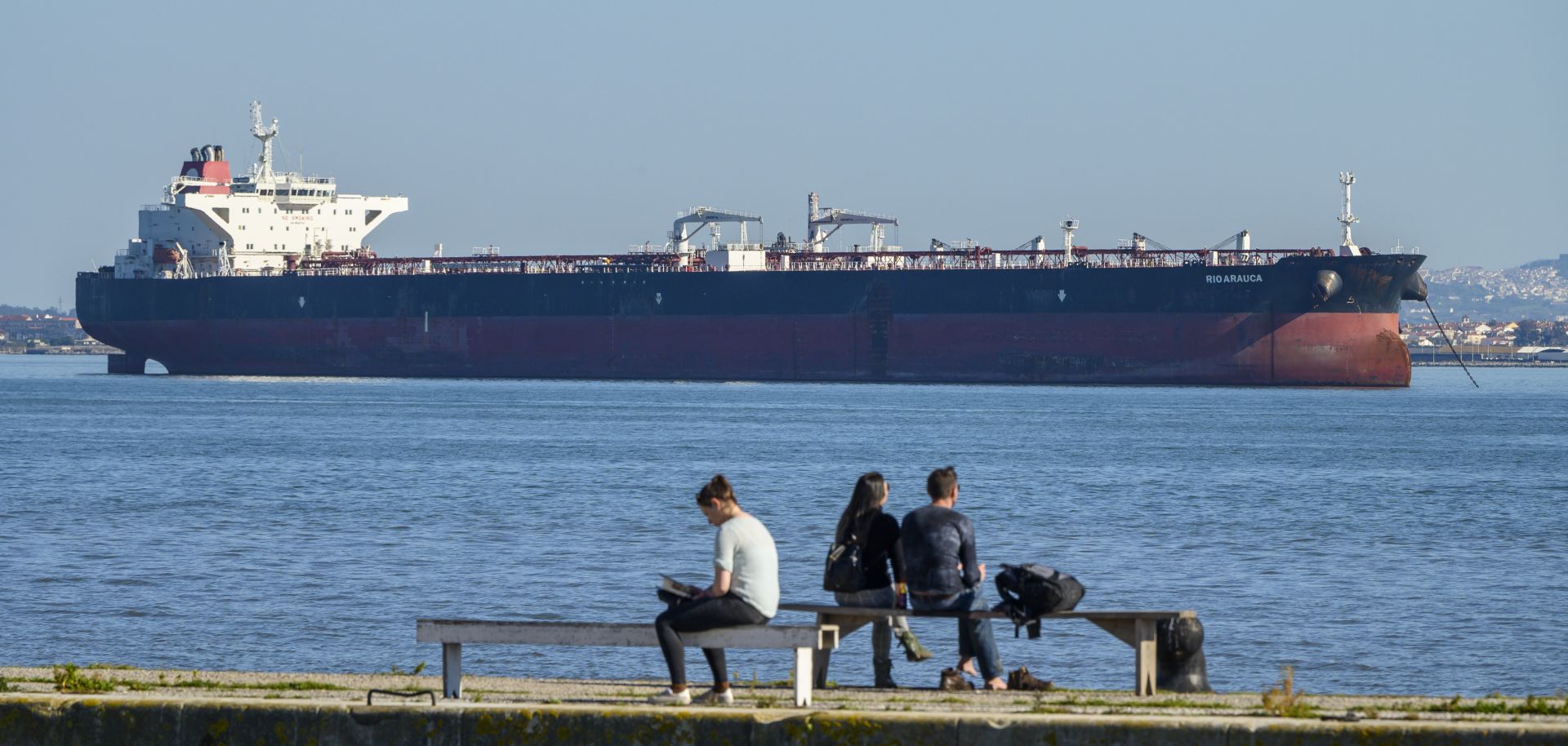 People relax on the bank of the Tagus River where Venezuelan PDVSA oil tanker Rio Arauca lies at anchor, having been impounded by Portuguese authorities for nearly two years due to unpaid debt, March 9.
