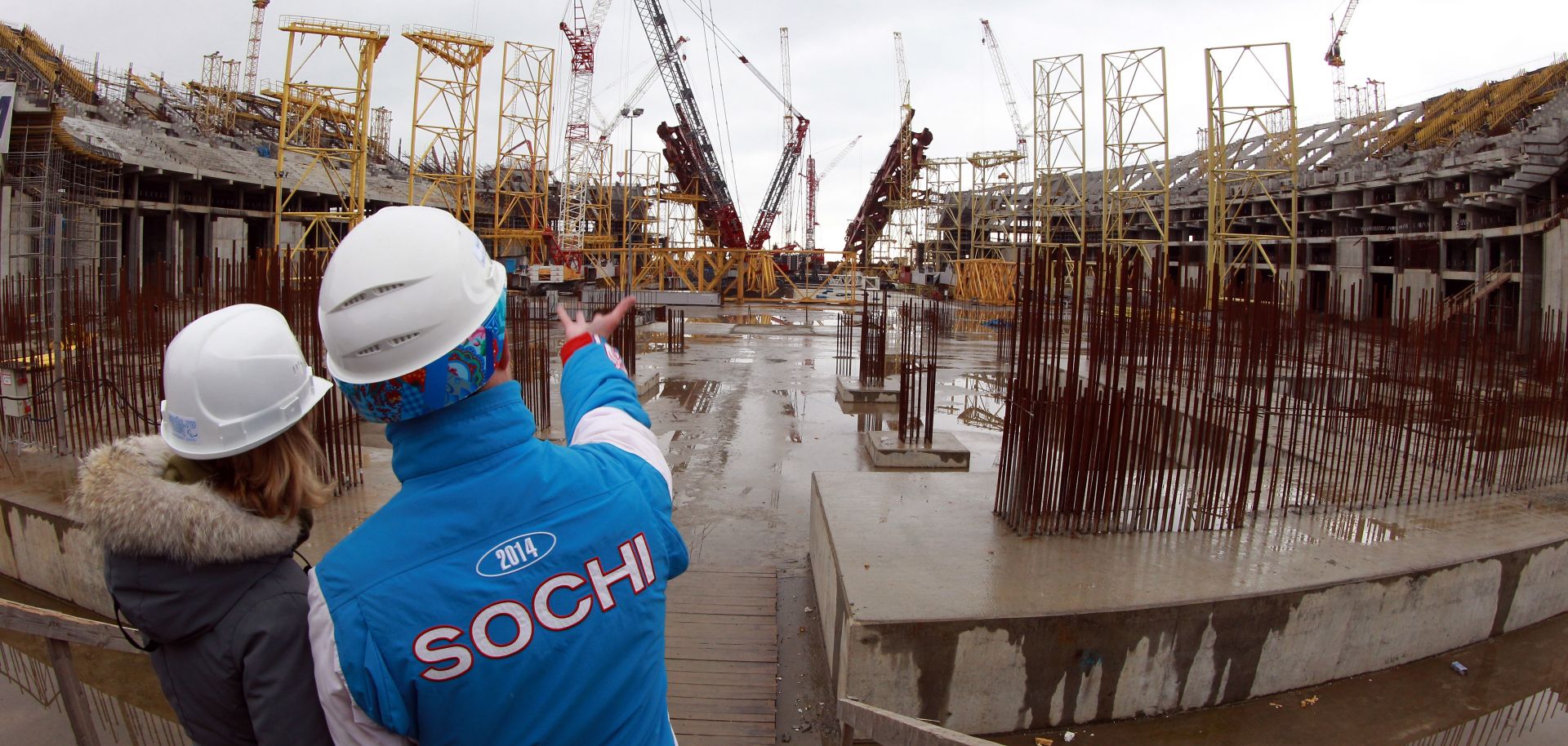 Volunteers stand on the ground of the construction site of the Olympic stadium.