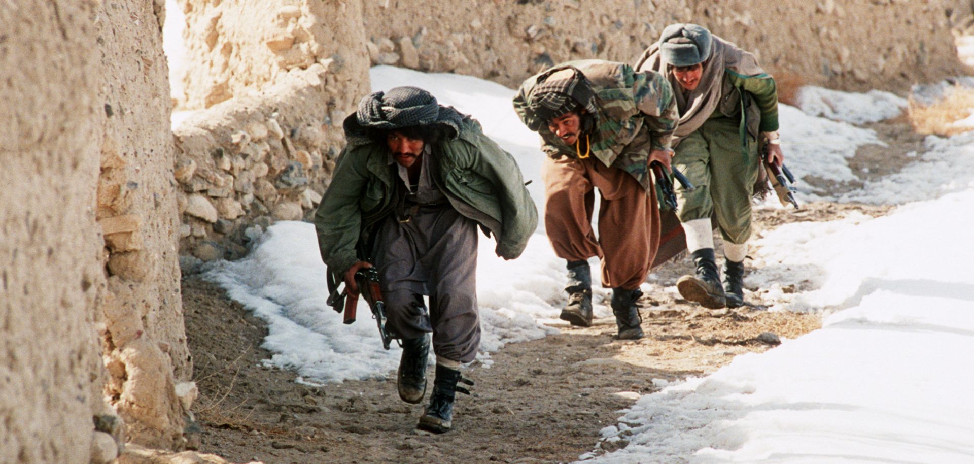 A group of Afghan mujahideen progress behind a wall in the village of Ghazni in southern Afghanistan as they fight Soviet-backed government forces in March 1989.