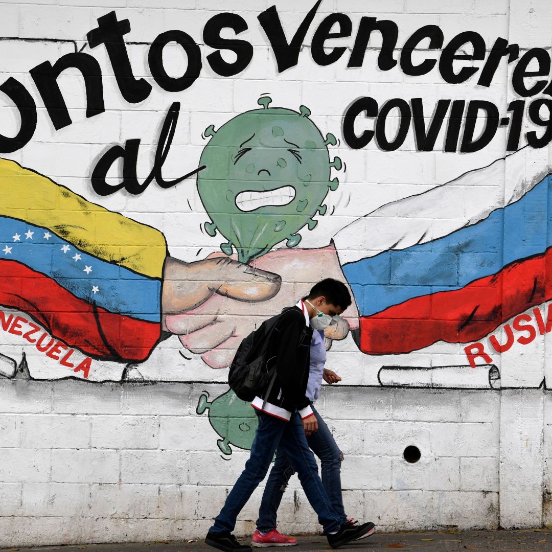 People walk past a mural of the Venezuelan and Russian flags that reads "Together we will defeat COVID-19" in Caracas, Venezuela, on March 4, 2021.