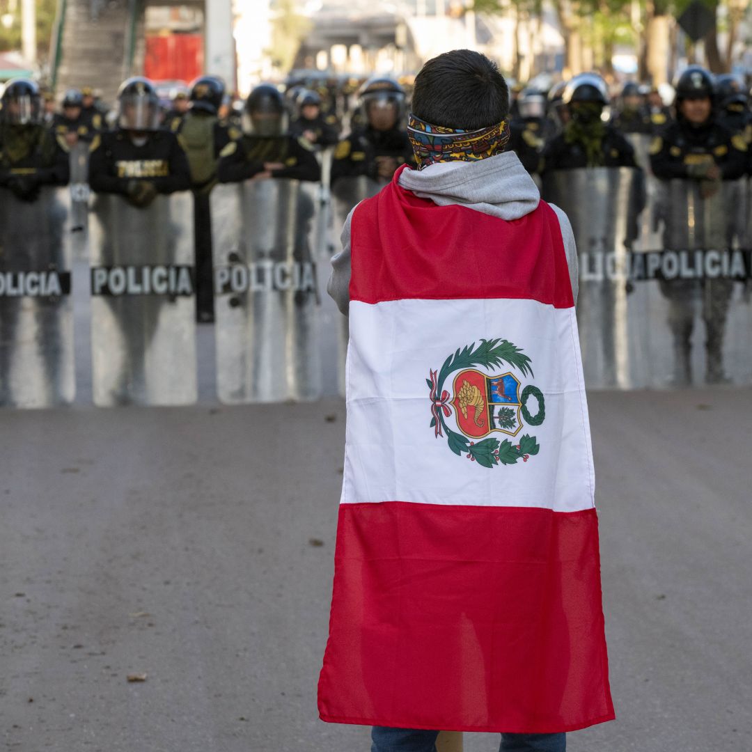 A demonstrator wearing the Peruvian flag stands in front of police officers forming a barrier with their riot shields near the entrance of the airport in Cusco, Peru, on Jan. 19, 2023.