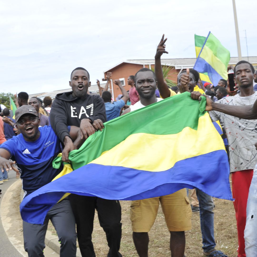 People hold up Gabon's national flag in the country's capital of Libreville on Aug. 30, 2023, as they celebrate after a group of military officers announced they were ''putting an end to the current regime'' and scrapping official election results that had handed another term to President Ali Bongo Ondimba. 